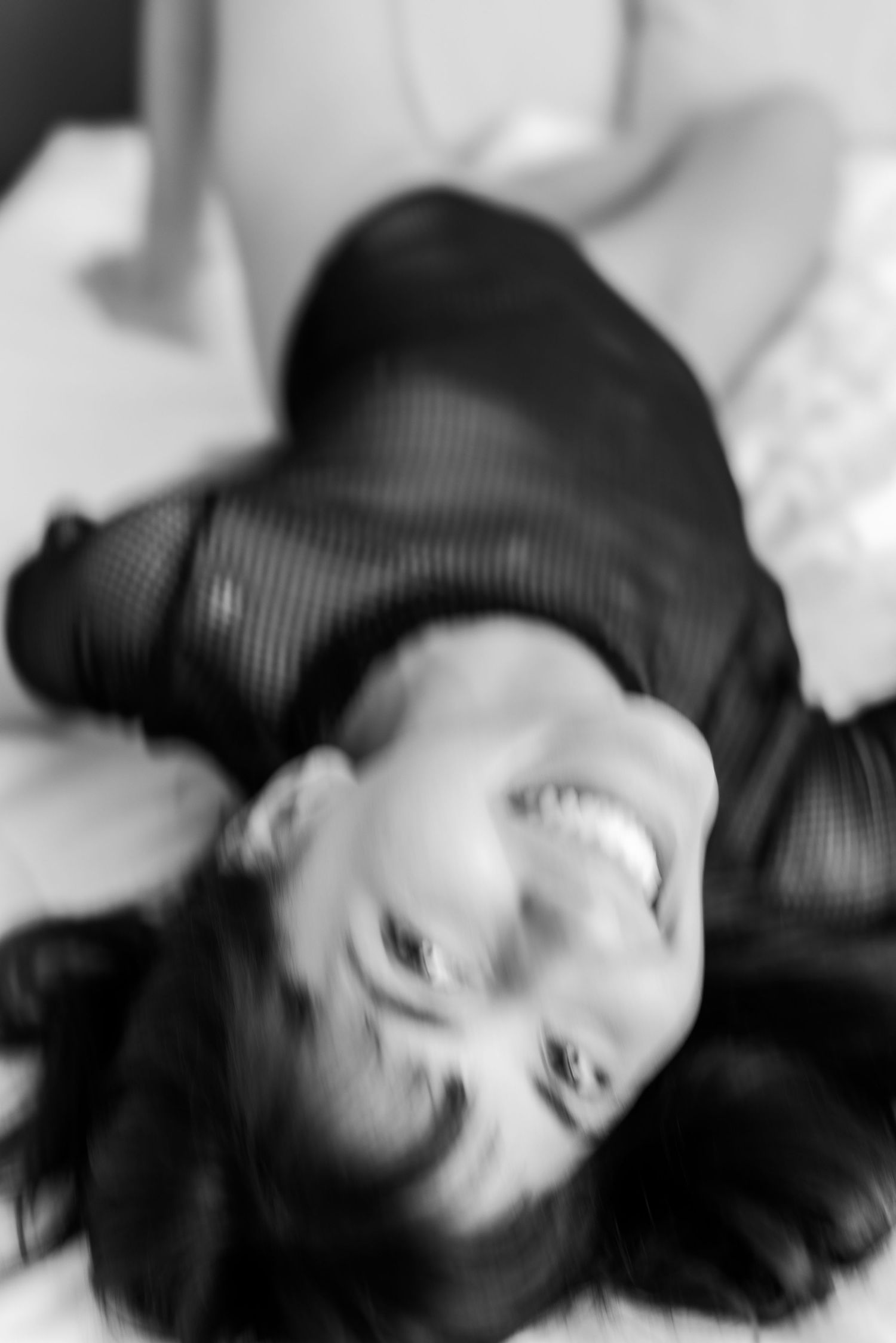 Black and white photo of someone laying down and laughing with long dark hair.