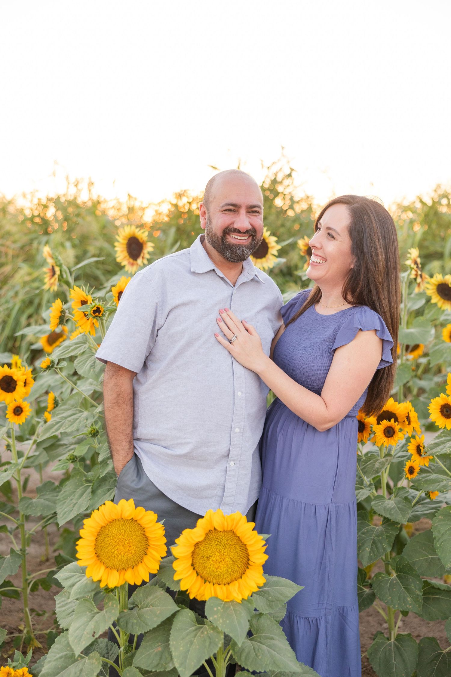 Couple smiling together in sunflower field during golden hour photography session.