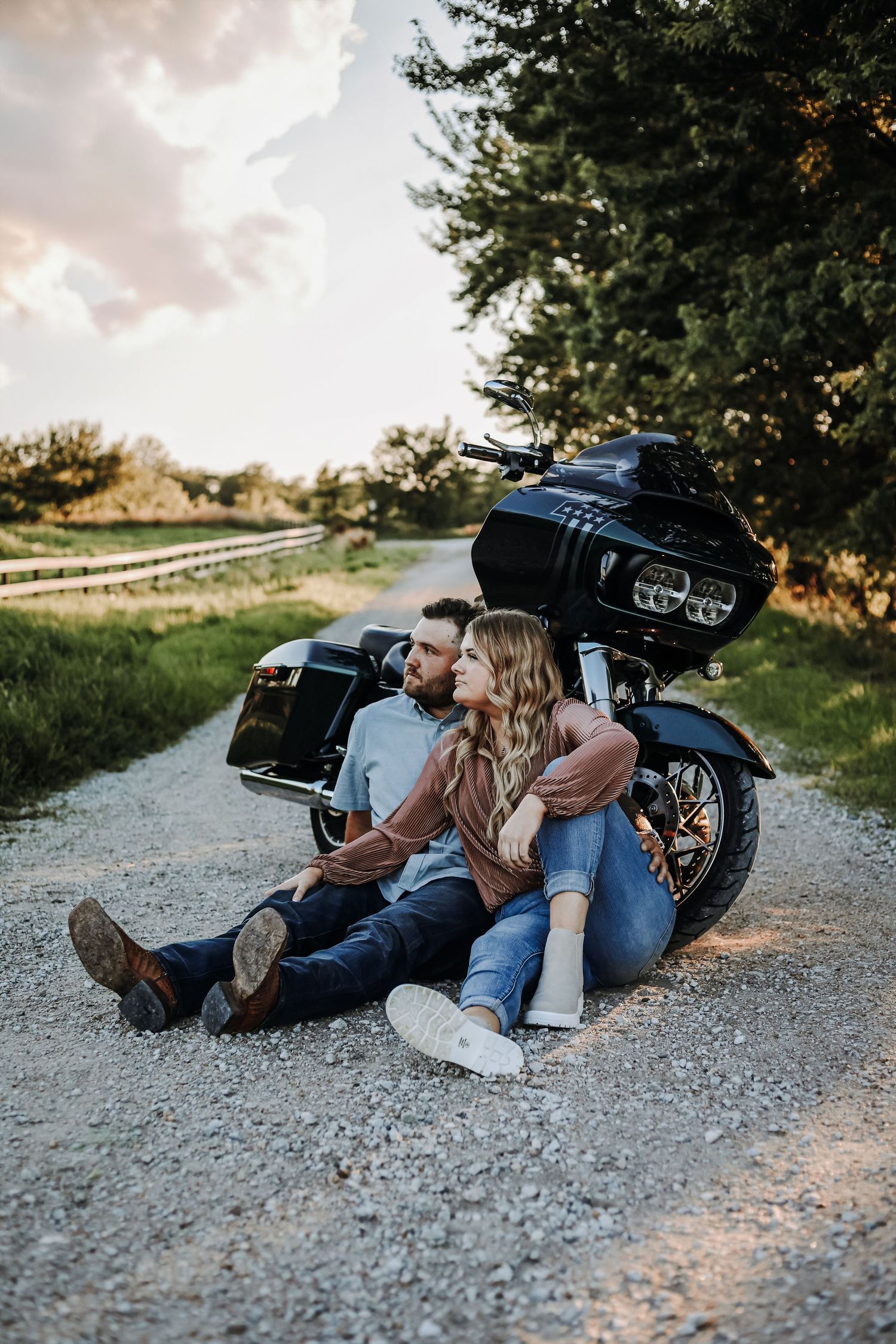 Couple relaxing on gravel path next to motorcycle during sunset photoshoot. Couples photography