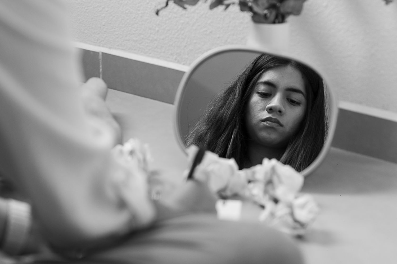 A circular mirror captures a monochromatic reflection with crumpled paper in the foreground.