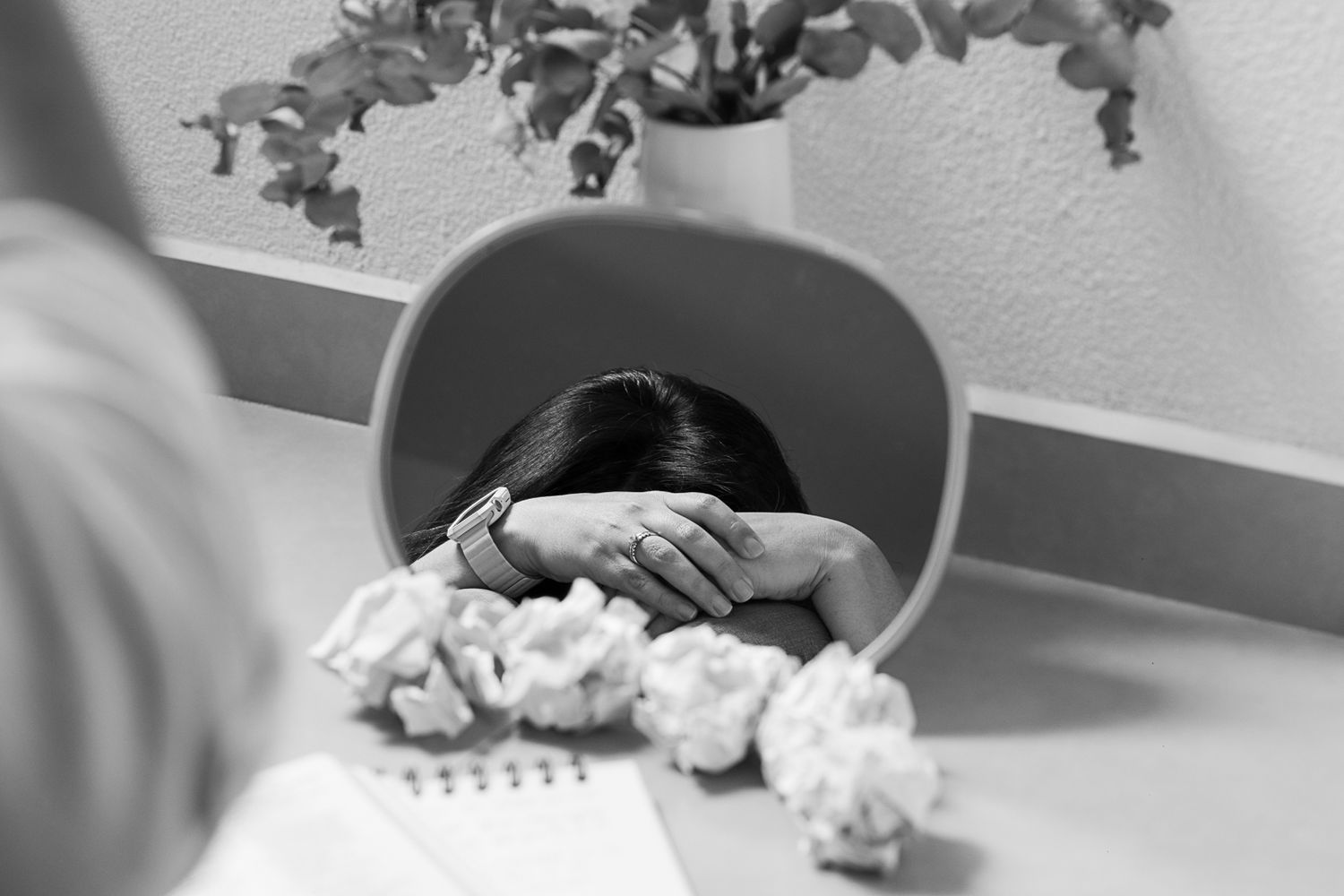 Black and white image of hands holding papers on a desk with a plant in the background.