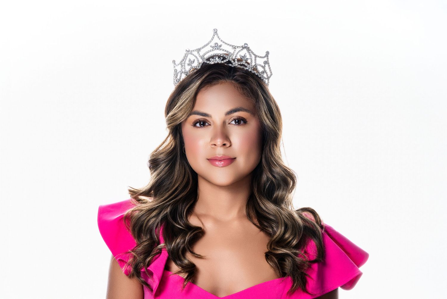 Portrait against white background wearing pink outfit and sparkling crown.