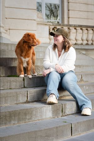 A Nova Scotia Duck Tolling Retriever sits on stone steps beside someone in casual attire.