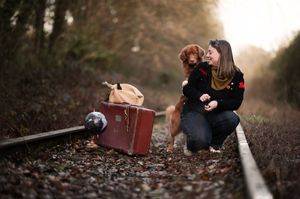 A vintage suitcase and camera sit on train tracks while figures crouch beside them in warm autumn lighting.