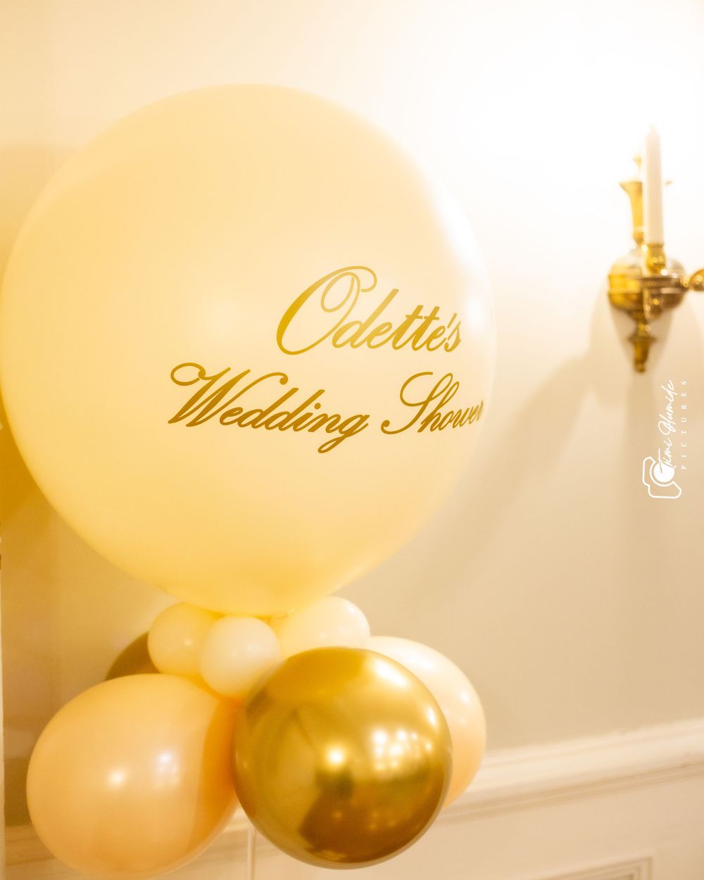 Gold and white balloons decorate a wedding shower event space with elegant text on the wall.