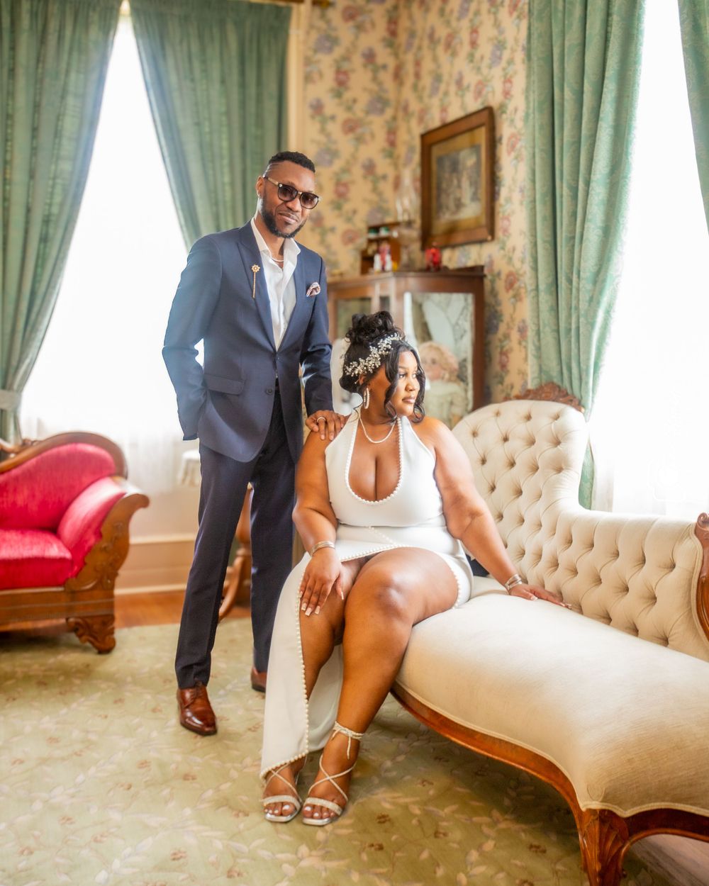 Stylish couple in formal attire posing in vintage-decorated room.