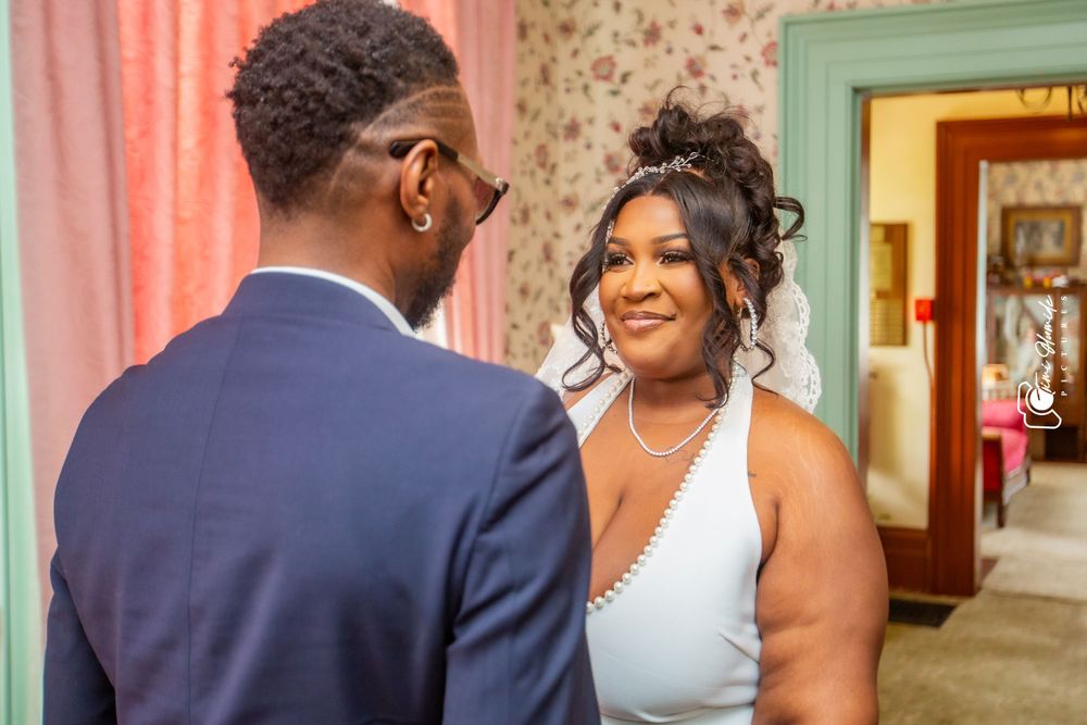 A tender moment between newlyweds in a room with floral wallpaper and soft lighting.