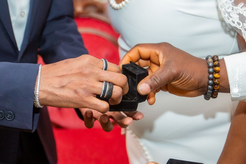 Close-up shot of hands exchanging wedding rings with a beaded bracelet visible.