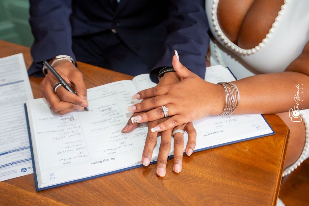 Newlyweds signing marriage documents with wedding rings visible on their hands.
