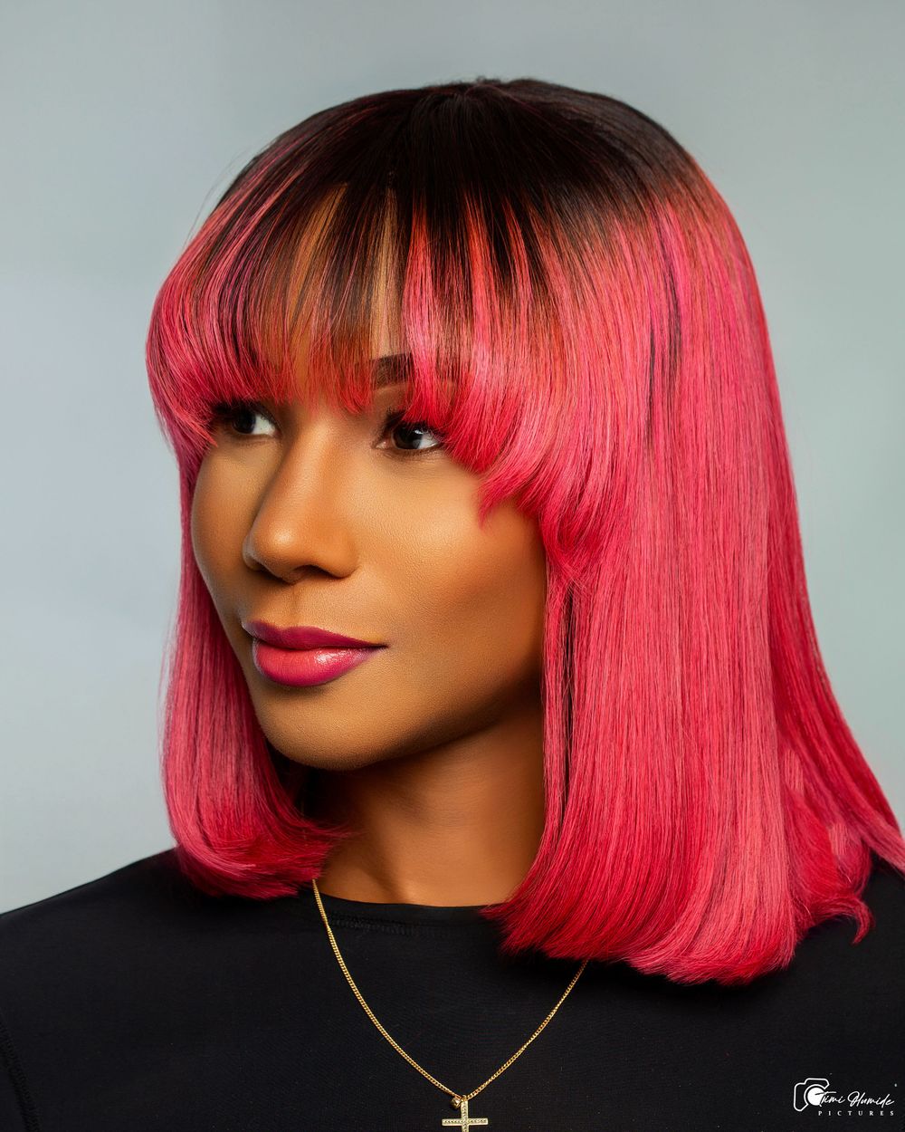 Studio beauty shot featuring bright red bob hairstyle with dark roots and gold cross necklace.