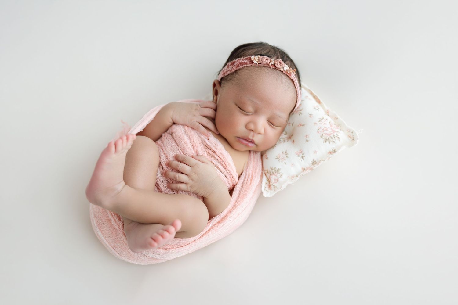 A sleeping baby nestled with a light blue blanket and small pacifier on white bedding.