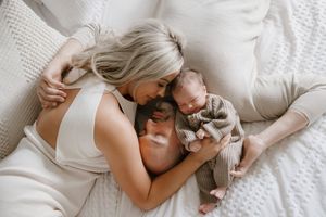 Family lying together on white bedding in soft, intimate portrait series.