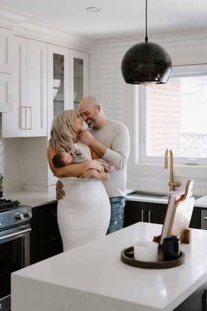 Intimate moment in a modern white kitchen with a baby being held between two adults.