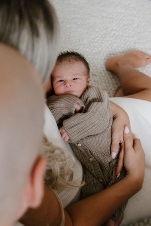 Close-up series of baby wearing knit sweater lying on white bedding.