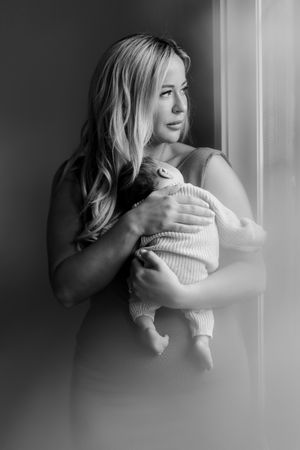 Black and white portrait of a baby being held near a window in soft natural light.