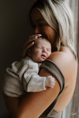 Intimate close-up of a sleeping newborn in a knit sweater being held against someone.