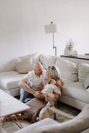 Cozy living room scene with a baby and adults sitting on a white sectional sofa.