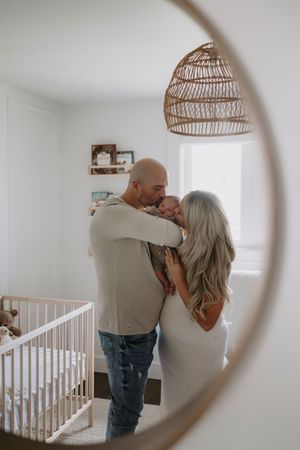 Family sharing intimate moments in nursery room viewed through circular frame.