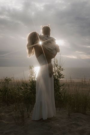 Backlit couple embracing against moody cloudy sky at dusk.