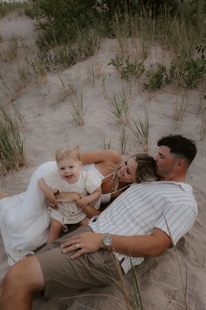 A family lies together on sandy dunes during a casual outdoor photoshoot.