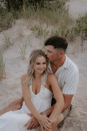 Couple in white clothing shares intimate moments on sandy beach dunes.