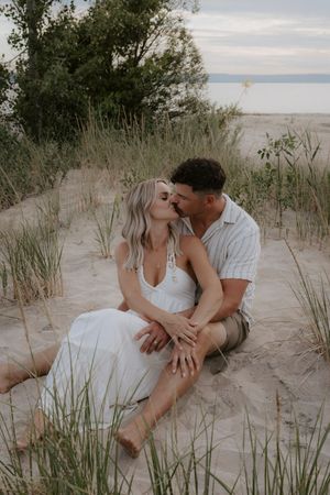 Romantic couple poses together on sandy beach during sunset photoshoot.