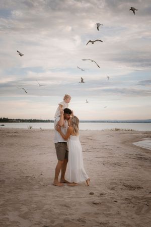 Family enjoys beach sunset with seagulls flying overhead.