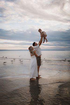 A couple plays in shallow ocean water at sunset with dramatic cloudy skies.
