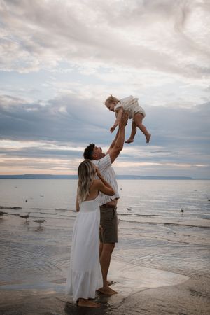 A family shares joyful moments together while standing in shallow beach water at dusk.