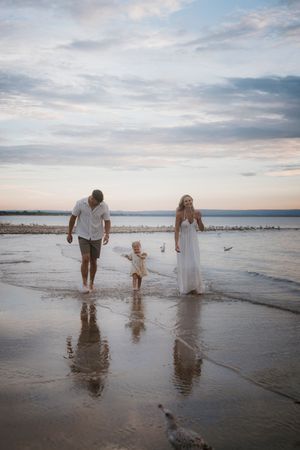 Family walking along shoreline at sunset creating reflections in wet sand.