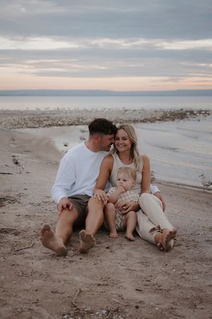 Family sits together on sandy beach during sunset.