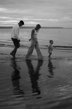 A family walks along the shoreline creating reflections in the wet sand at sunset.