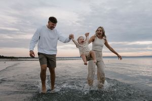 A family plays and splashes together in shallow water at the beach during sunset.