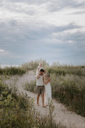Couple walking along a sandy path through coastal vegetation.