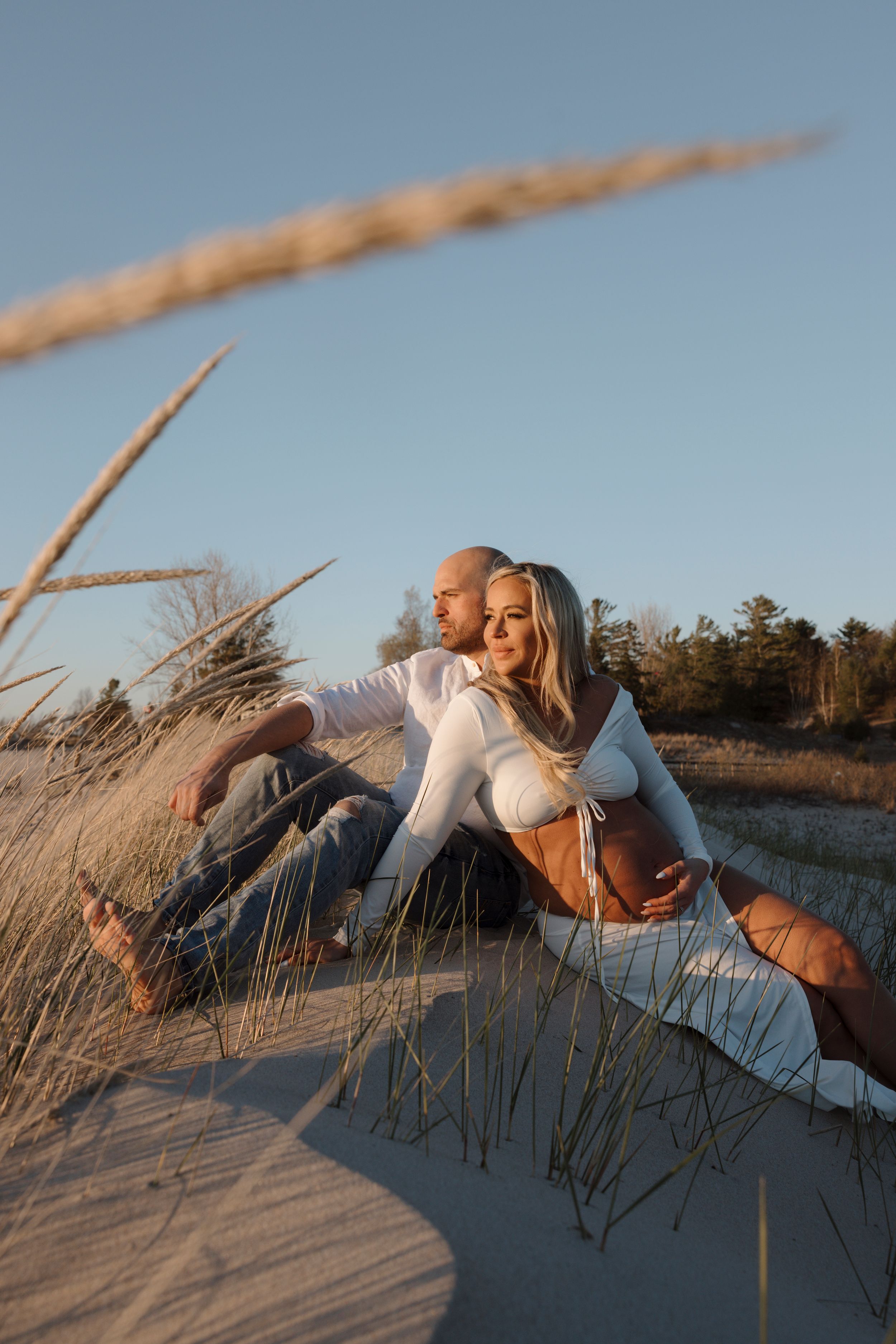Couple shares intimate moment on sandy beach during golden hour maternity session.