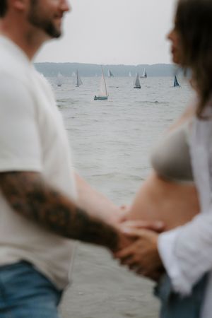 A romantic moment captured on a beach with sailboats dotting the misty horizon in the background.