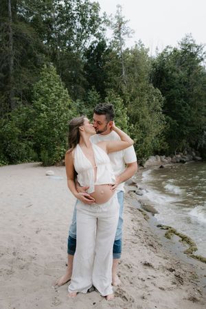 Couple embracing on a sandy beach with trees and greenery in the background.