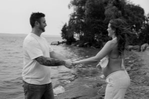 Dancing together on a beach shoreline with water and trees in view.