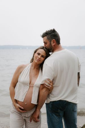 Intimate black and white portrait of a couple embracing on a cloudy beach.