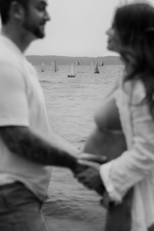 People walking along a misty beach with sailboats in the distance.