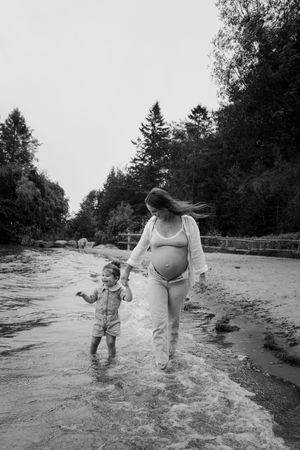 Family playing together in shallow water at beach with evergreen trees in background.