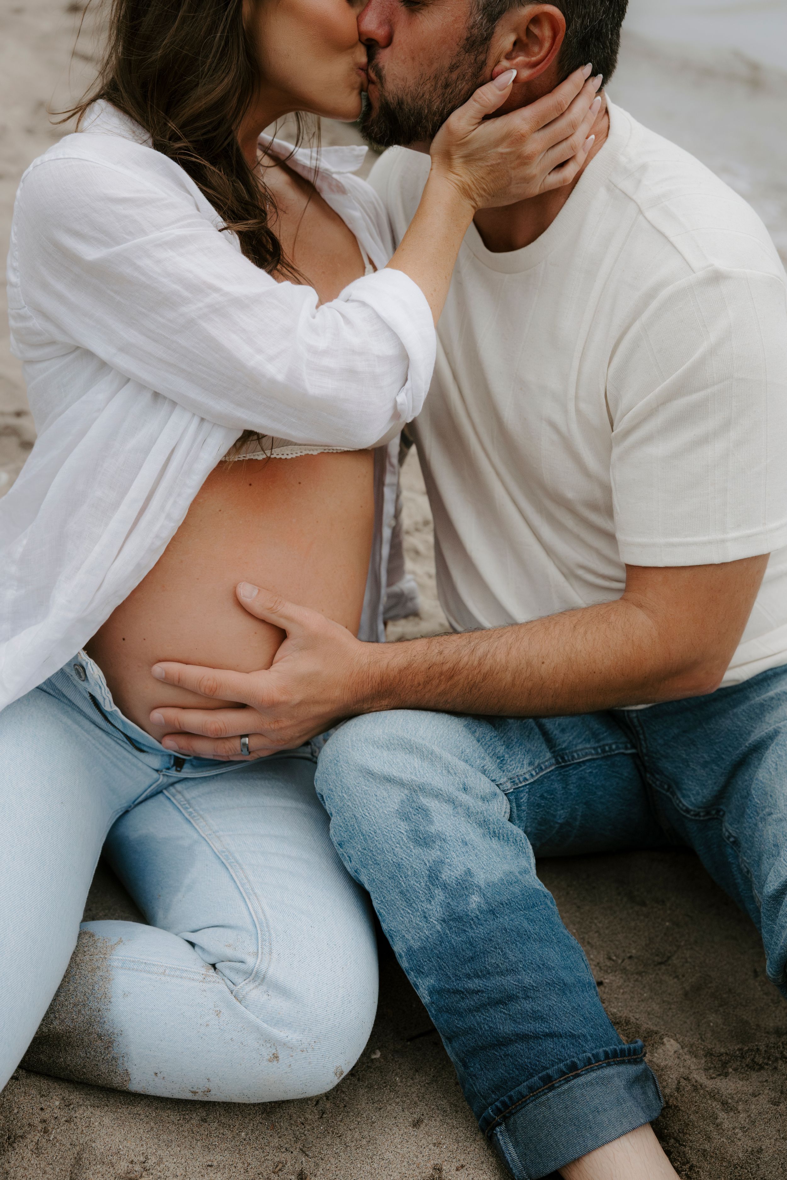 Intimate couple sharing romantic moment on beach wearing white and denim.