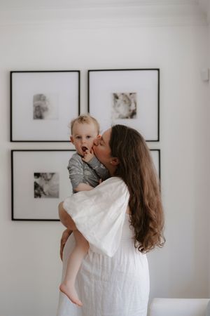 Parent and baby share joyful embraces against a minimalist white wall with black framed art.