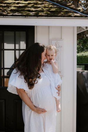 Sweet interactions between family members wearing white dresses against white exterior wall.