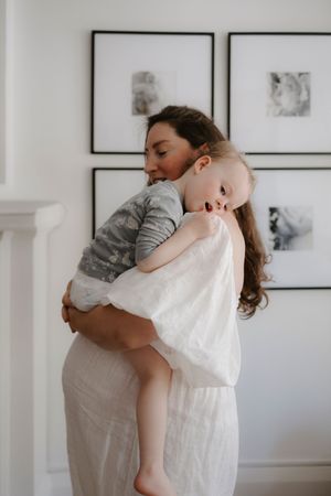 Tender embrace between parent and child in minimalist white room with framed artwork.