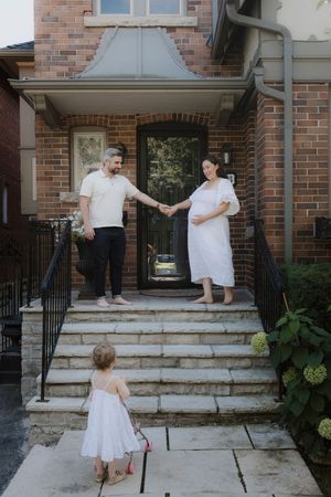 Family in white clothing sharing tender moments on brick house front steps.