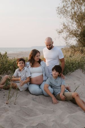 A family relaxes together on sandy dunes during a maternity photoshoot.