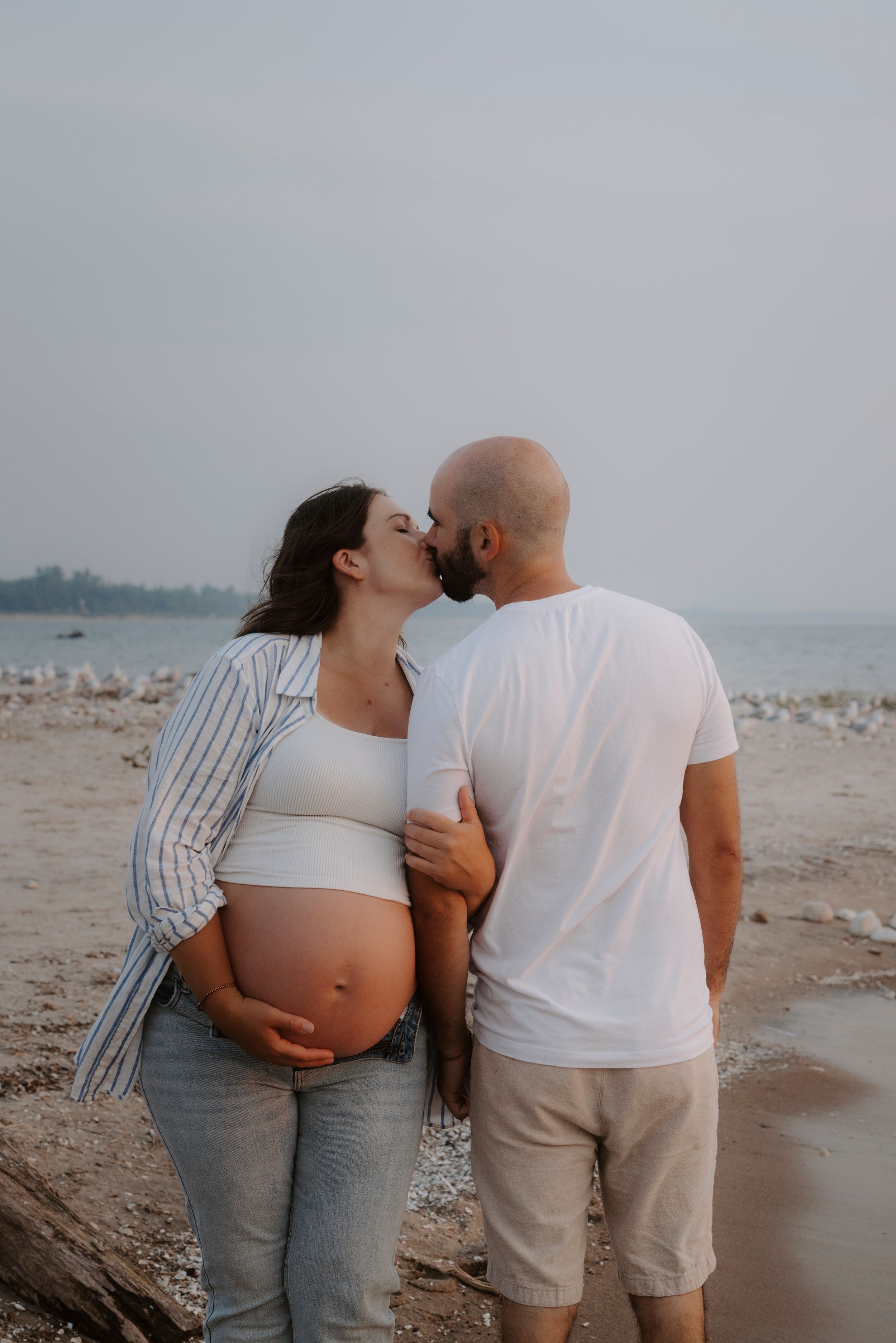 Romantic maternity beach photos with couple in casual attire against ocean backdrop.