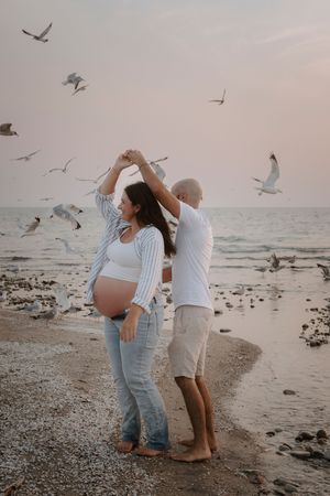 Family maternity photos on beach with seagulls flying overhead at sunset.