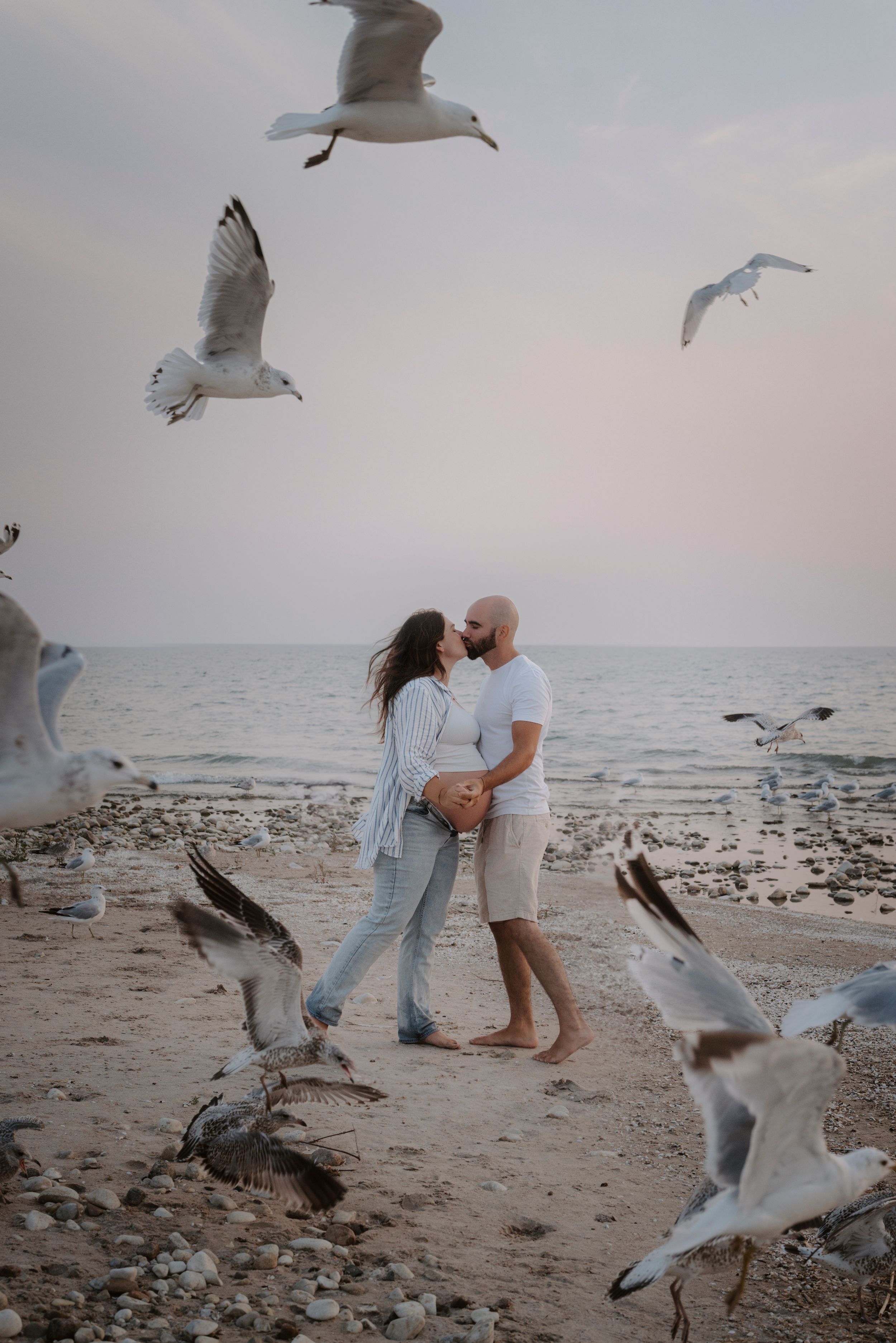 Beach maternity photos with seagulls flying around couple during golden hour.